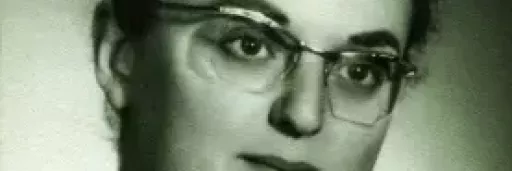 Black-and-white portrait of Judit Kinszki wearing glasses, with dark hair pinned up, looking slightly to the side against a plain background.