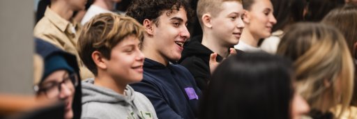 A group of young students sitting in an audience, smiling and listening attentively during a presentation or seminar.