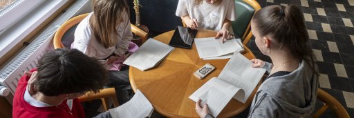 Four School Students sitting together at a round wooden table, discussing a reader's text