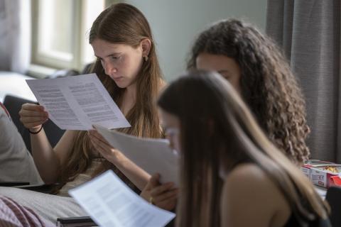 Three girls sitting together in a seminar room, reading documents