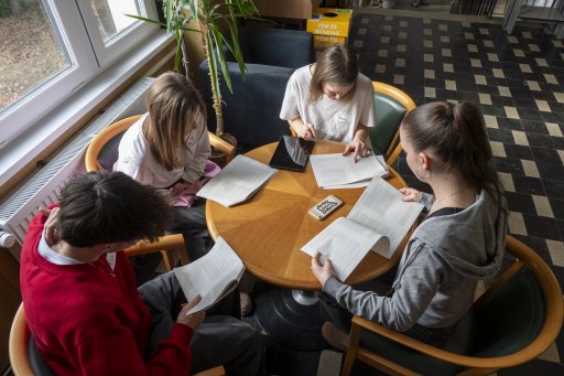 Four School Students sitting together at a round wooden table, discussing a reader's text